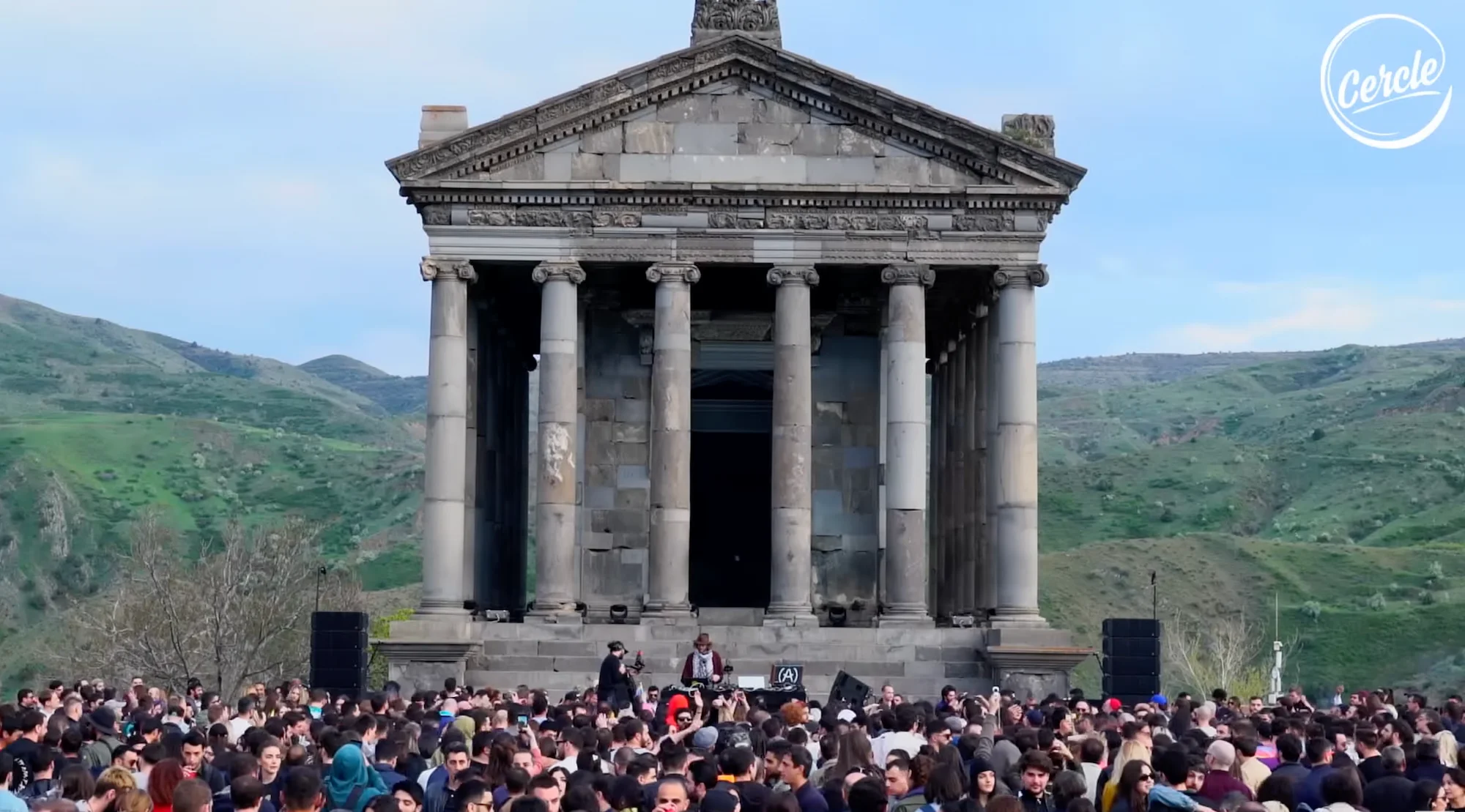 A Cercle DJ set and crowd in front of the colonnaded Greco-Roman Temple of Garni in Armenia, with mountains behind.