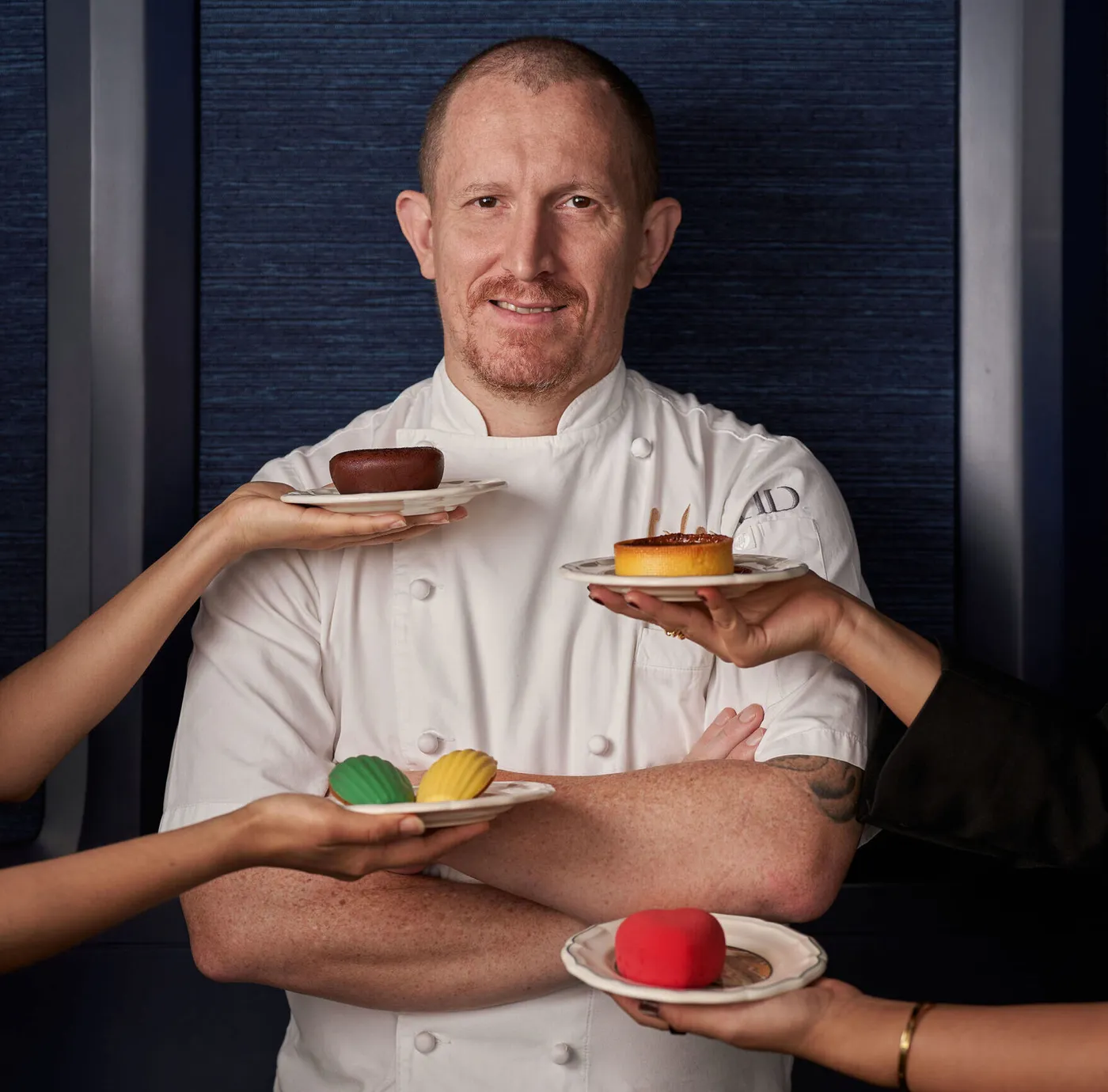 Executive Pastry Chef Christophe Grilo holding plated desserts at Blue by Alain Ducasse