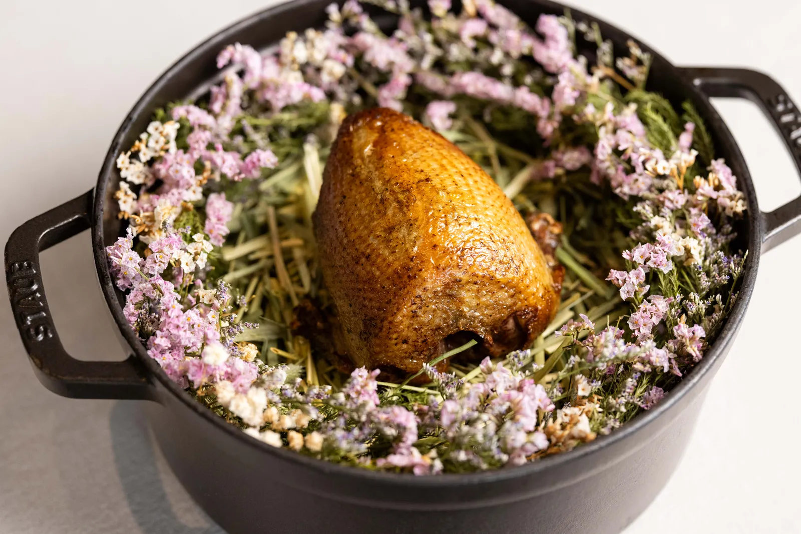 Dry-aged pigeon served in a cast-iron cocotte with flowers, summer 2026 menu at Blue by Alain Ducasse