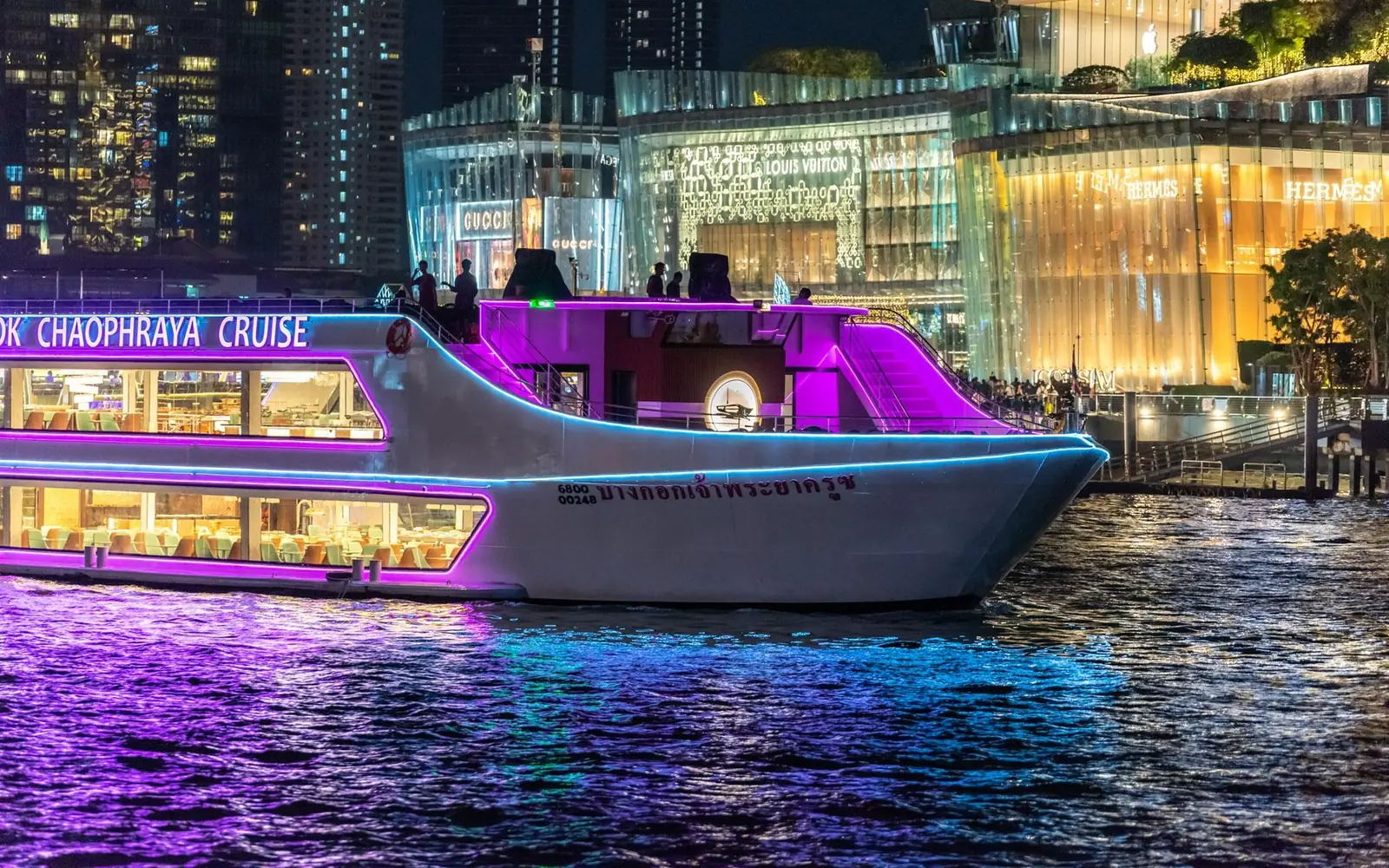 The Bangkok Chaophraya Cruise boat lit in purple neon on the river in front of ICONSIAM at night