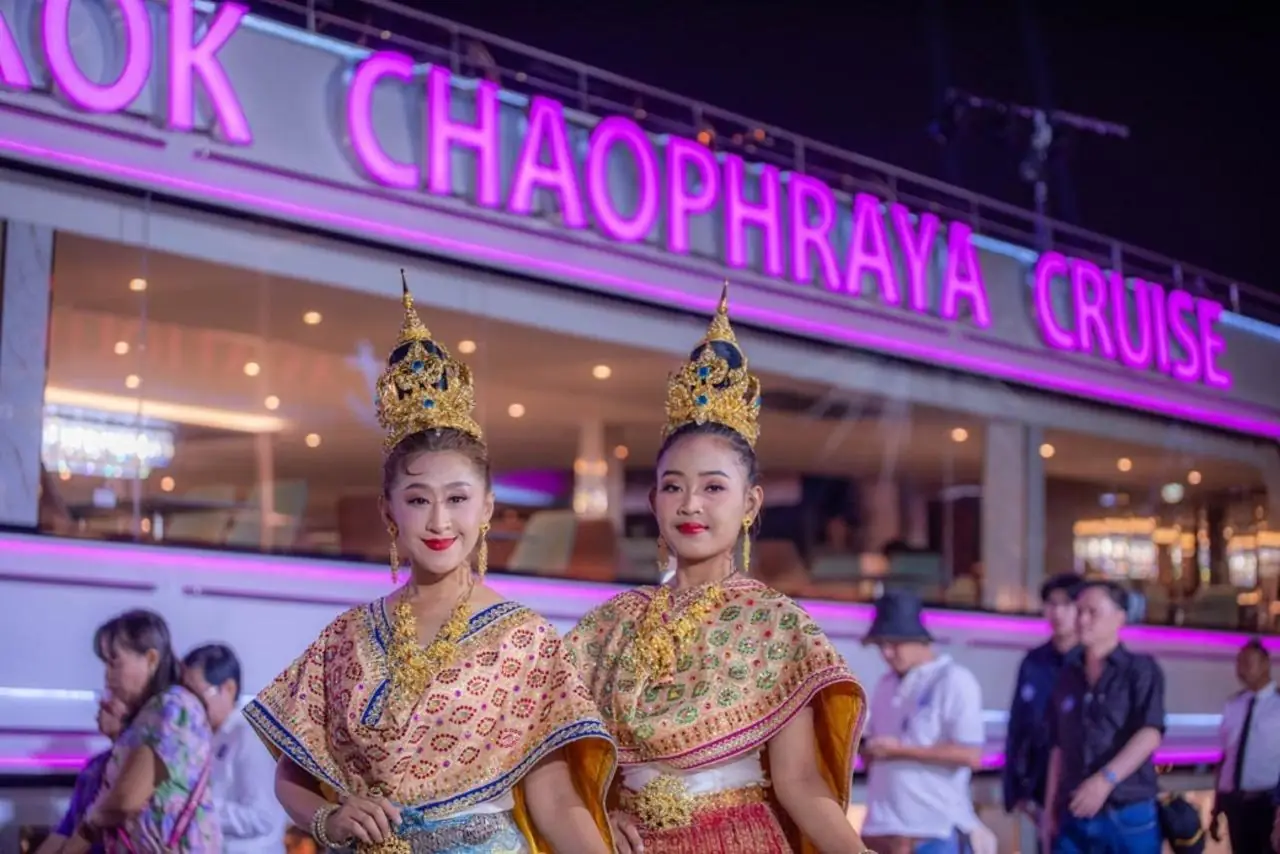 Two hostesses in Thai costume beside the boat at night, its neon name above them