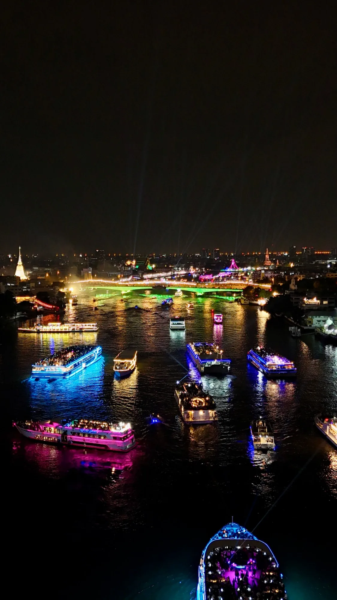 Lit-up dinner cruise boats on the Chao Phraya at night, with a bridge and temples lit up behind