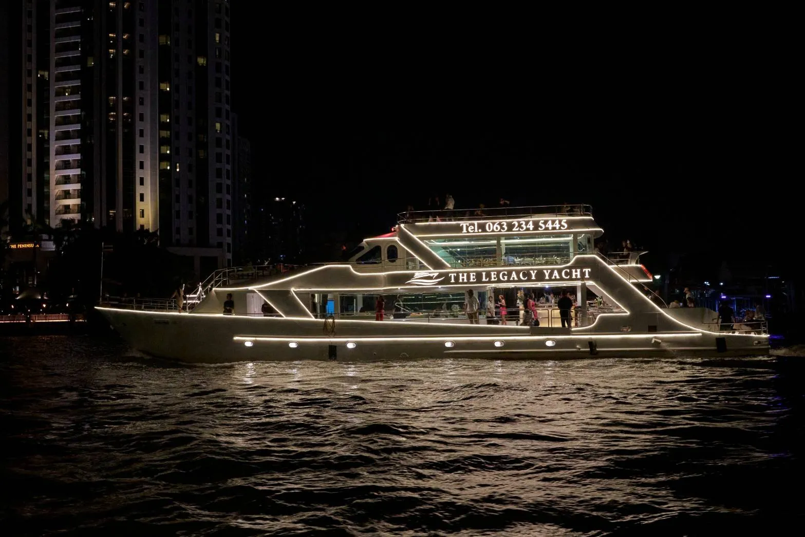 The Legacy Yacht lit up on the Chao Phraya at night, guests on its two decks