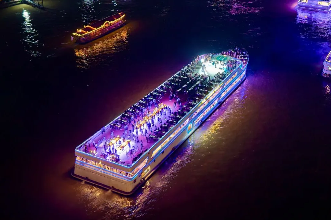 The Luxury White from above at night, its top deck lit up in purple and full of diners