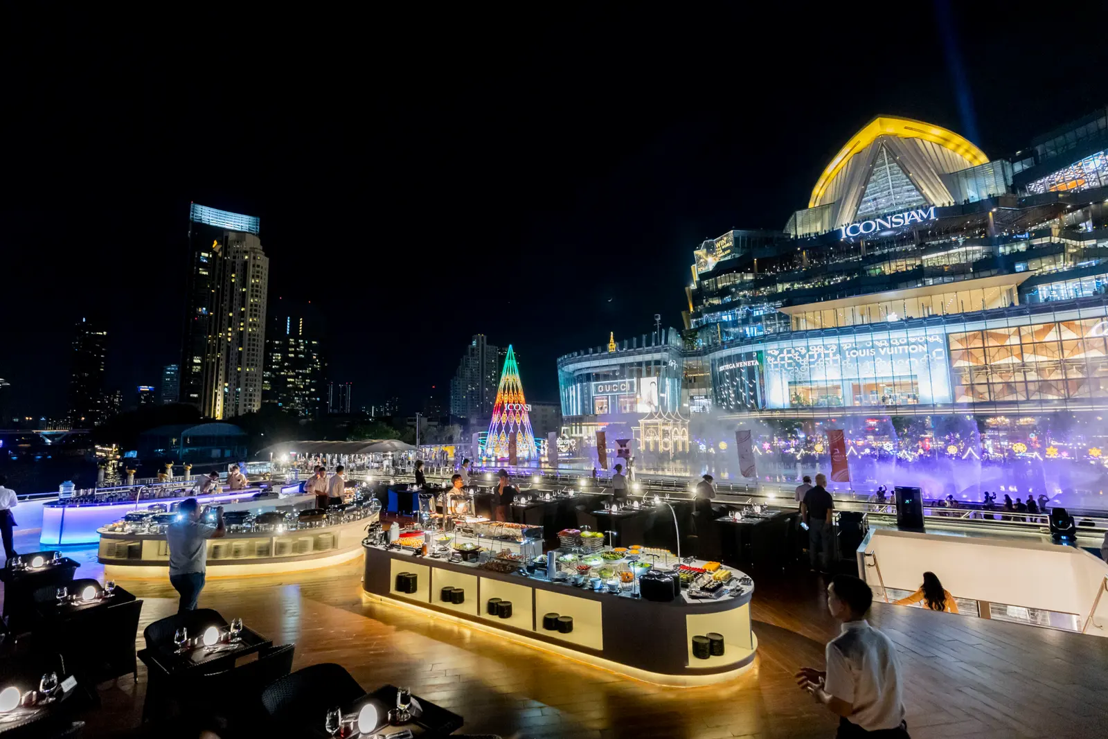 Buffet counters and tables on the open rooftop of The Opulence, facing ICONSIAM at night