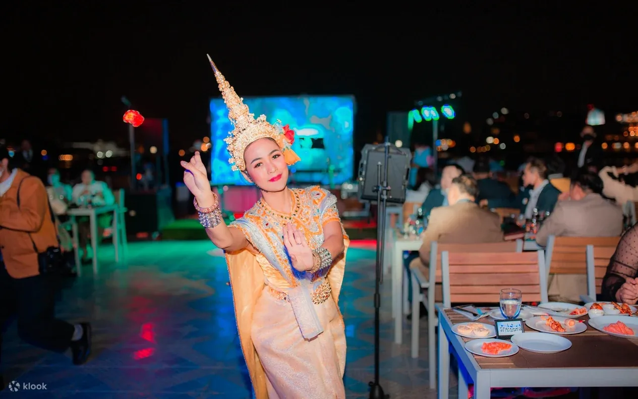 A Thai classical dancer performing between the dinner tables on the deck of the Smile Riverside cruise at night