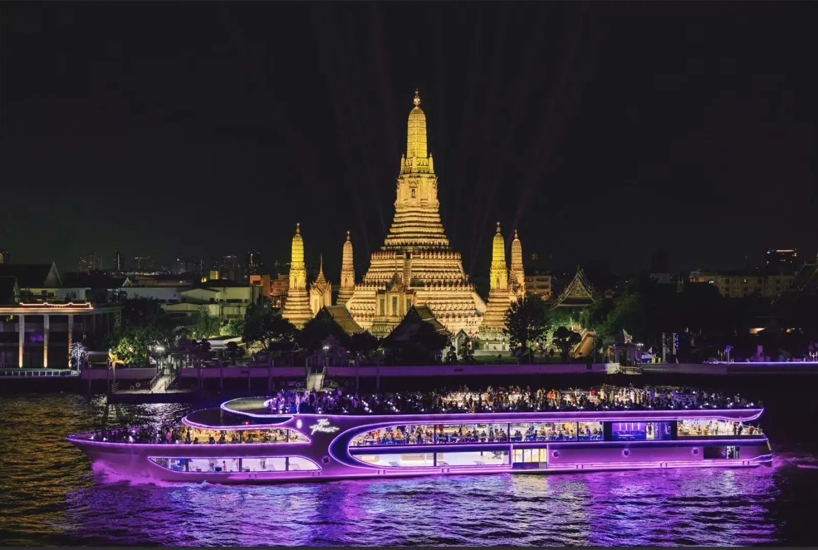 The Planet Cruise glowing purple on the river at night, with Wat Arun behind