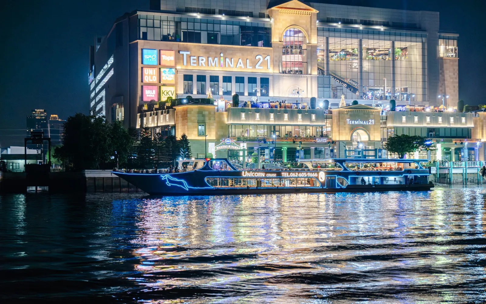 The Unicorn Cruise boat full of guests on the Chao Phraya in front of Terminal 21 Rama 3 at dusk