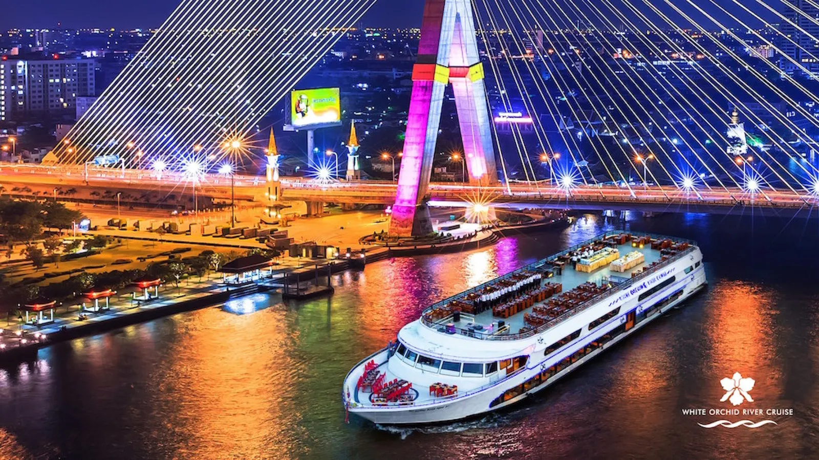 The White Orchid cruise boat under the lit-up Rama VIII bridge at night