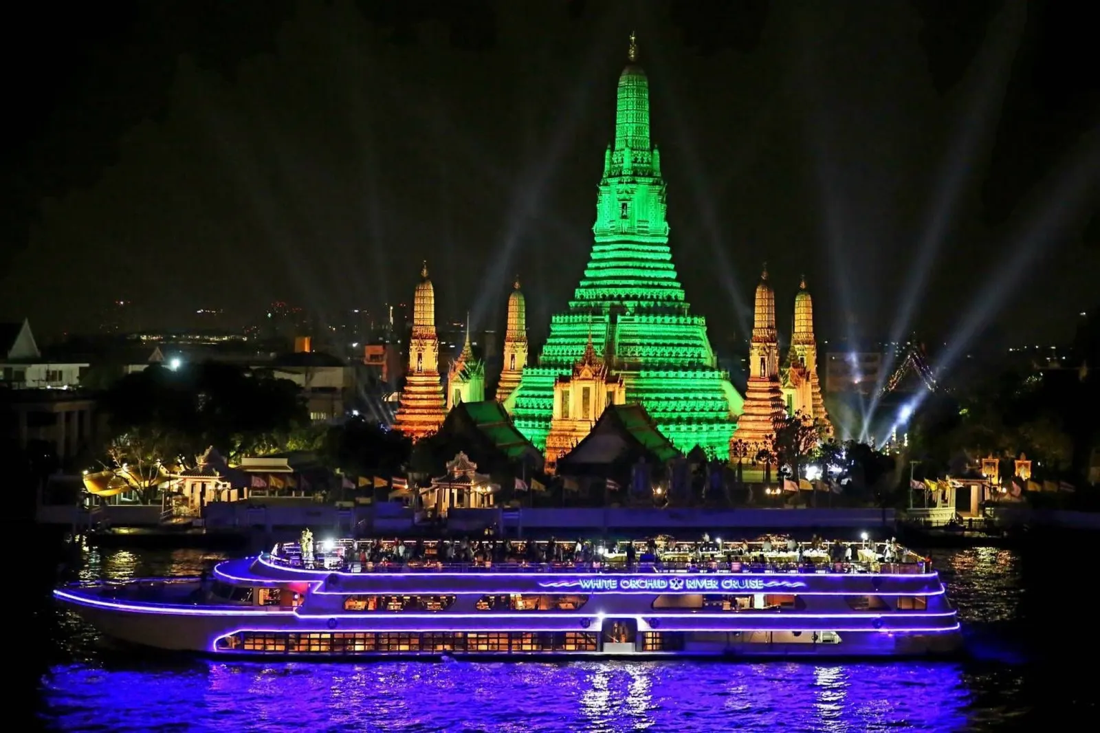 The White Orchid cruise boat lit up in blue in front of Wat Arun at night
