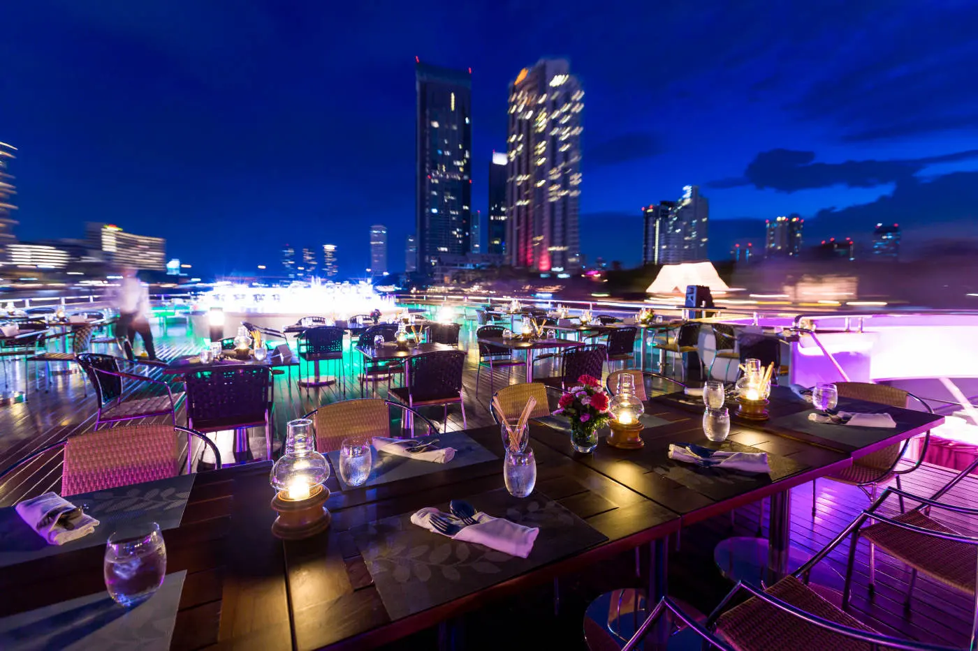 Candlelit tables on the open-air deck of Wonderful Pearl at night, with riverside towers behind