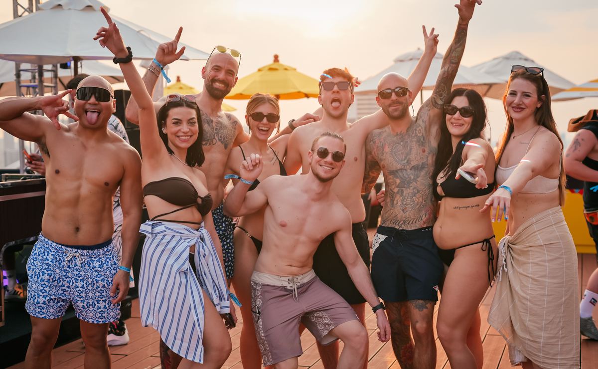 Guests cheering at the camera on the pool deck in the late afternoon sun at a Bangkok Rooftops pool party