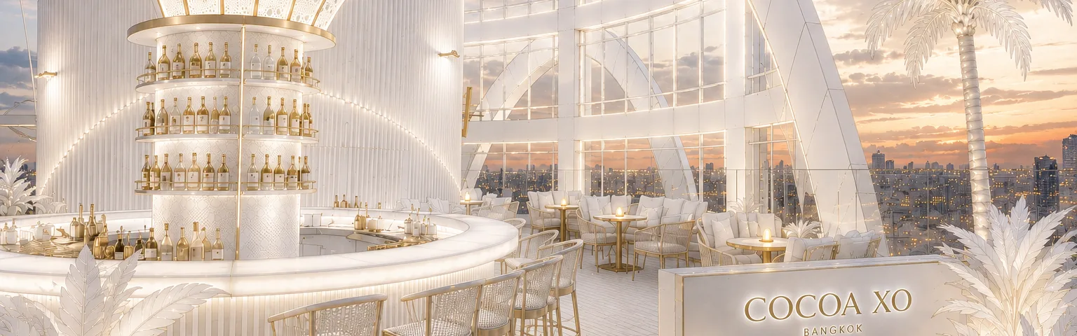 The white and gold interior of COCOA XO, its circular bottle-lined bar and arched windows opening onto the Bangkok skyline at sunset