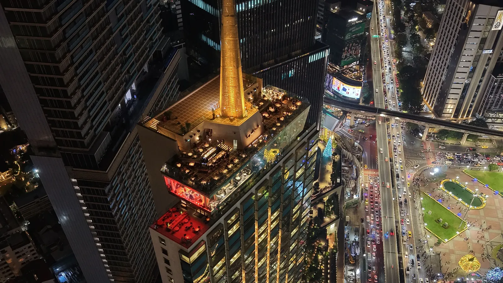 Night view of Spire rooftop on the Dusit Thani Bangkok, with the hotel's golden spire and Lumpini Park alongside