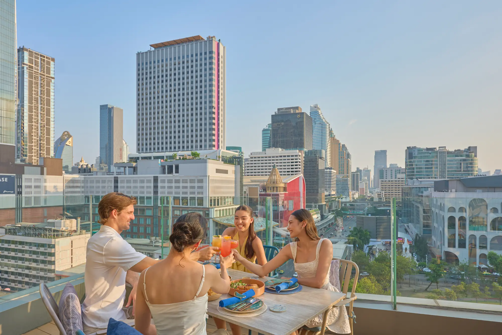Friends toasting cocktails on the View rooftop with the CentralWorld district skyline behind, Bangkok