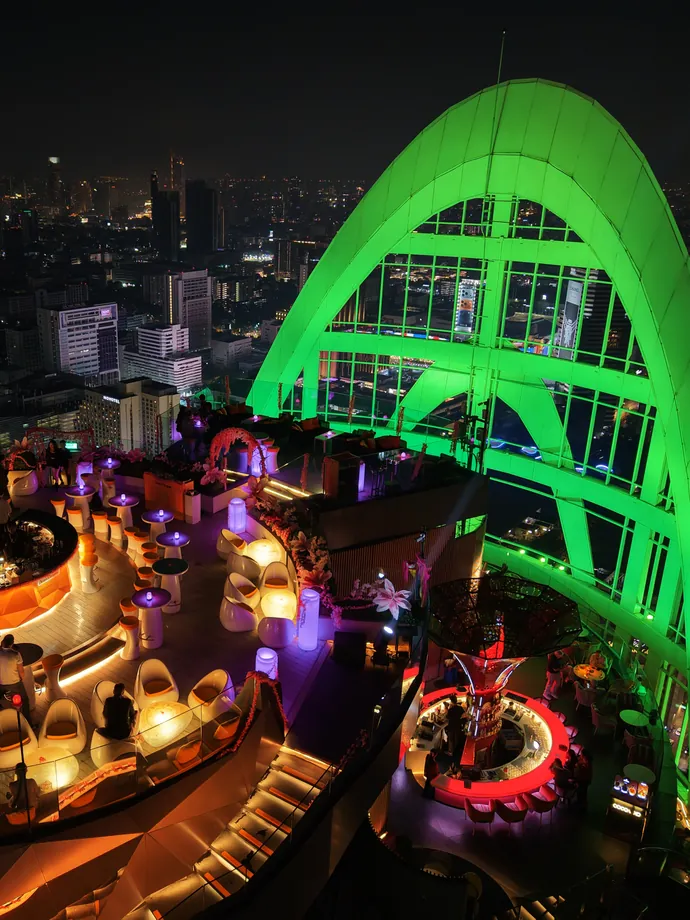 A rooftop lounge at the top of Centara Grand at CentralWorld at night, under an arch lit green