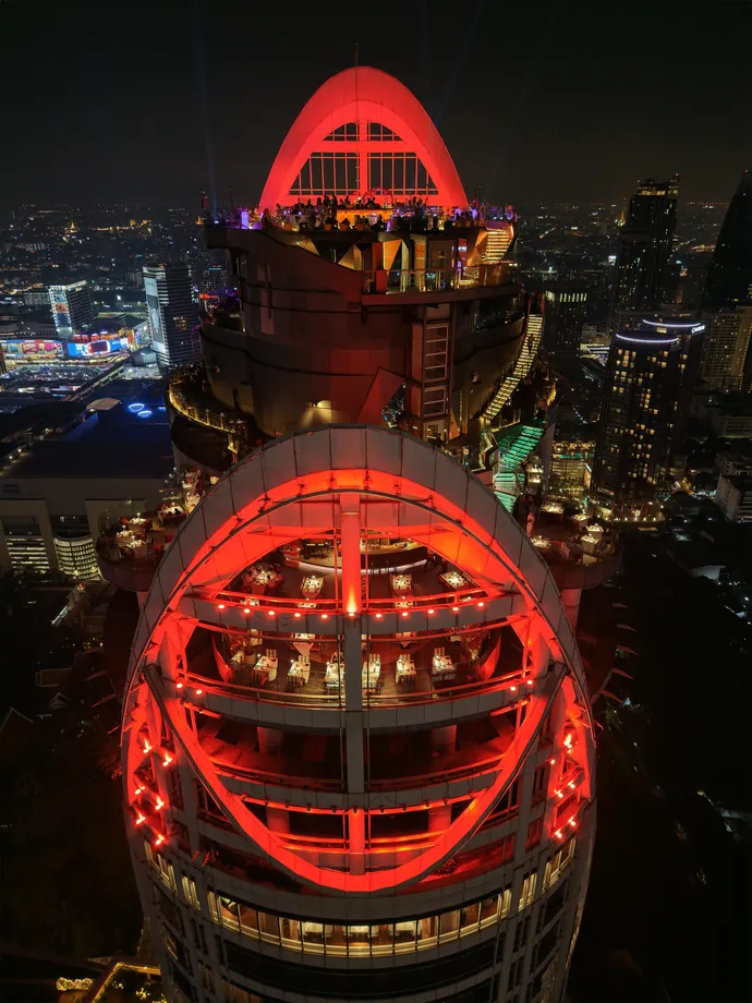 The top of Centara Grand at CentralWorld at night, its two rooftop arches lit red