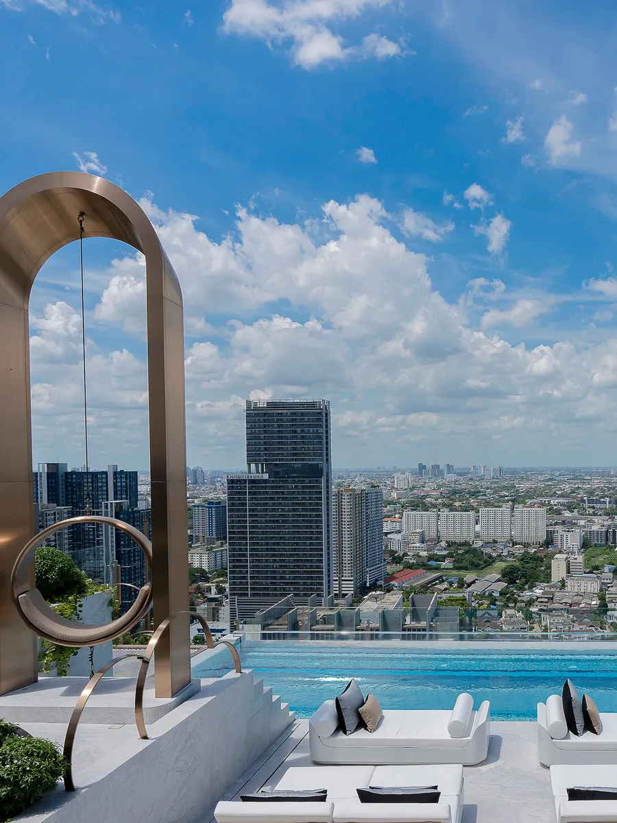 The 34th-floor infinity pool of INNSiDE by Meliá Bangkok Sukhumvit by day, a bronze arch and the city behind