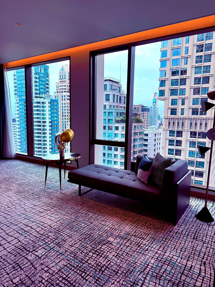 A suite living area at Kimpton Maa-Lai Bangkok, a chaise in front of floor-to-ceiling windows onto the city