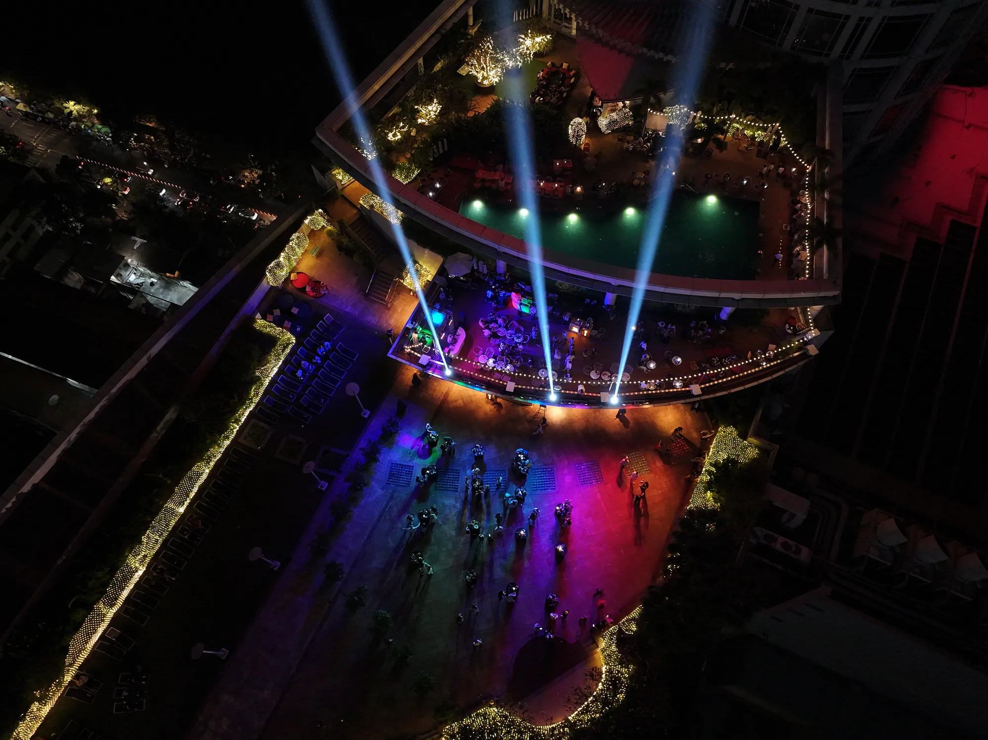 The 26th-floor pool deck of Centara Grand after midnight on New Year's Eve 2025, light beams over the stage and the garden