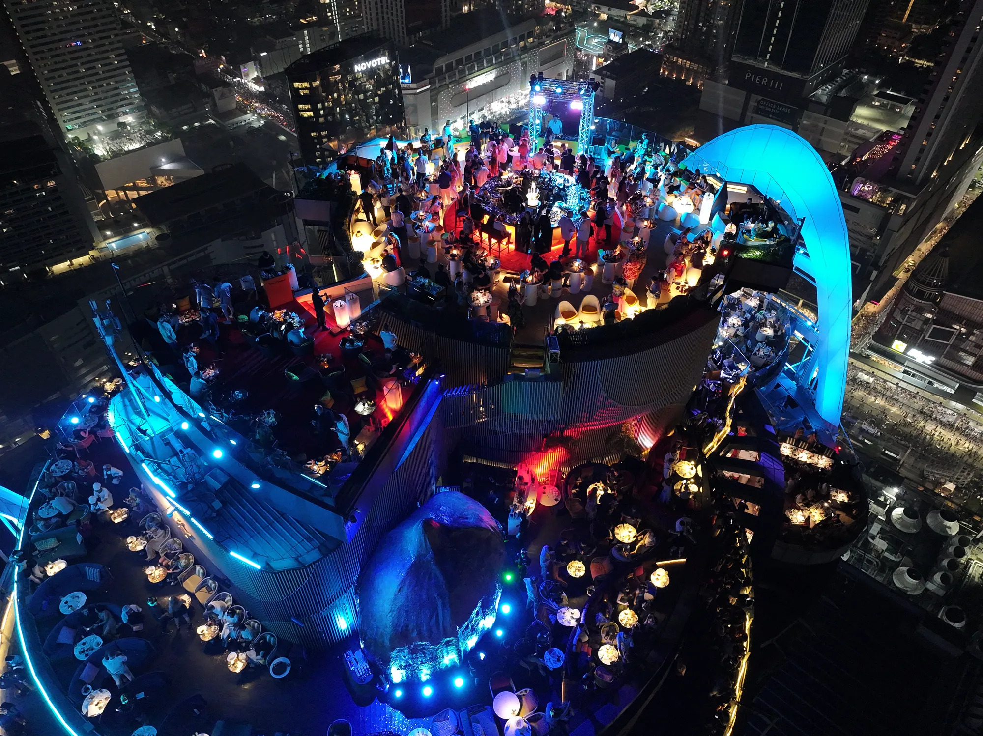 The Red Sky terraces laid for New Year's Eve 2025, tables full, the arch lit blue, from above after midnight