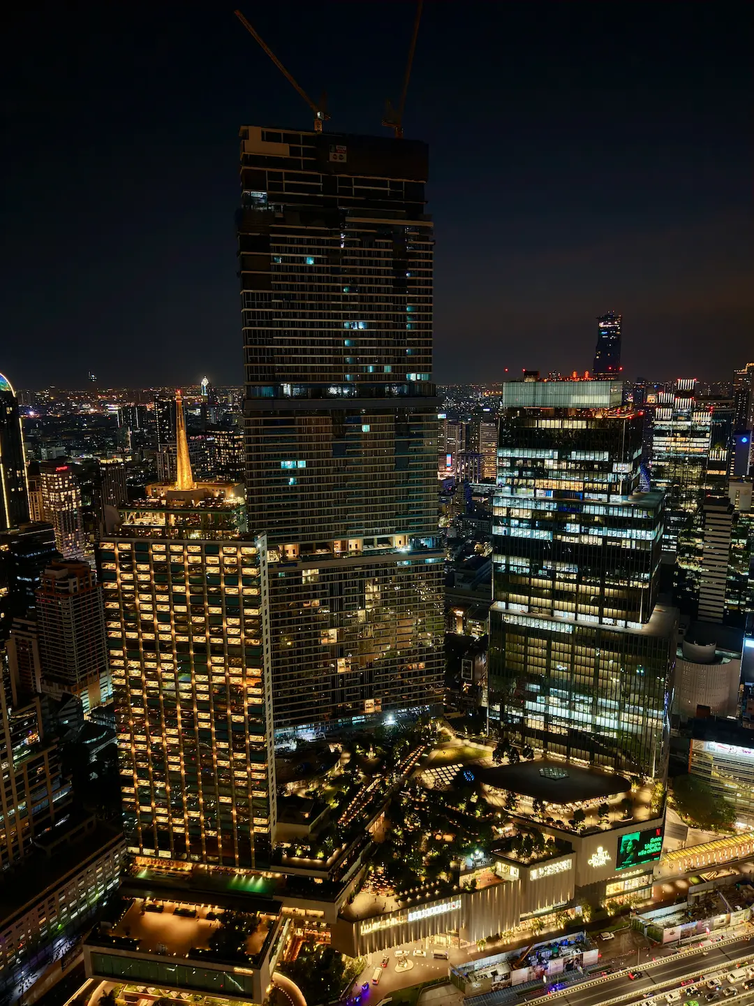 Night view of the Dusit Central Park towers beside Aether: the Dusit Thani hotel, the Dusit Residences and the Dusit Central Park offices, lit up