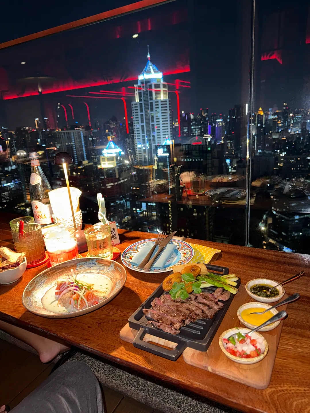 Dinner at a Bar.Yard window table, a grill board and sharing plates with the lit skyline behind