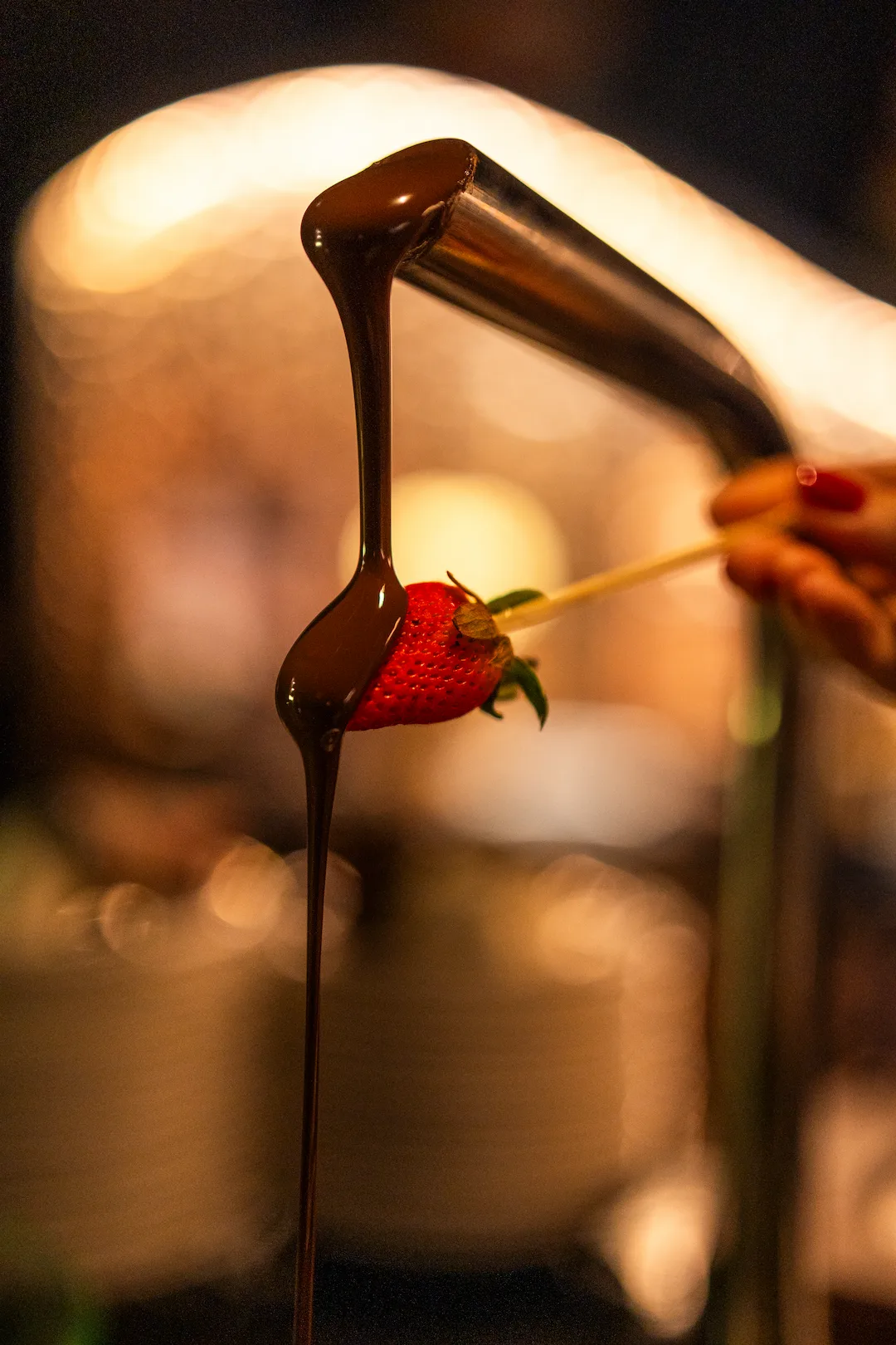 A fresh strawberry being dipped in flowing chocolate at the Cocoa XO chocolate fountain
