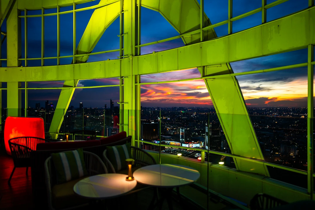 The green-lit steel frame of the Cocoa XO terrace with candlelit tables opening onto a fiery sunset over the Bangkok skyline