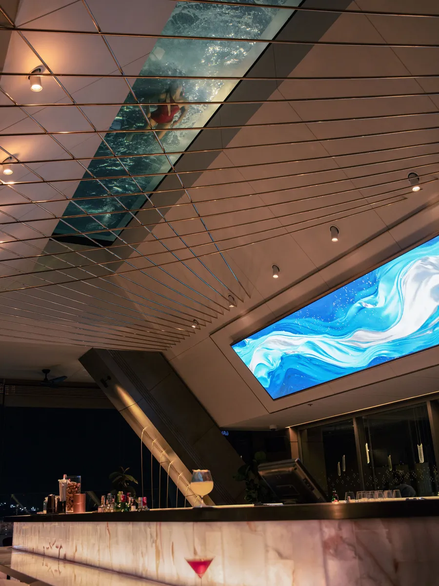 The bar counter at LUZ Bangkok Tapas Bar, with a swimmer visible through the glass bottom of the infinity pool above