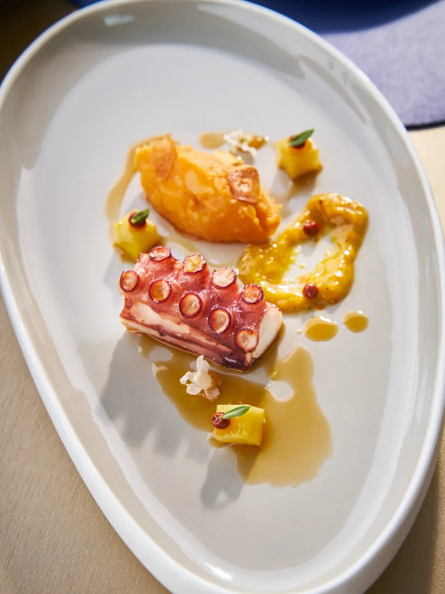 An octopus tentacle with orange purée on a white plate at LUZ Bangkok Tapas Bar