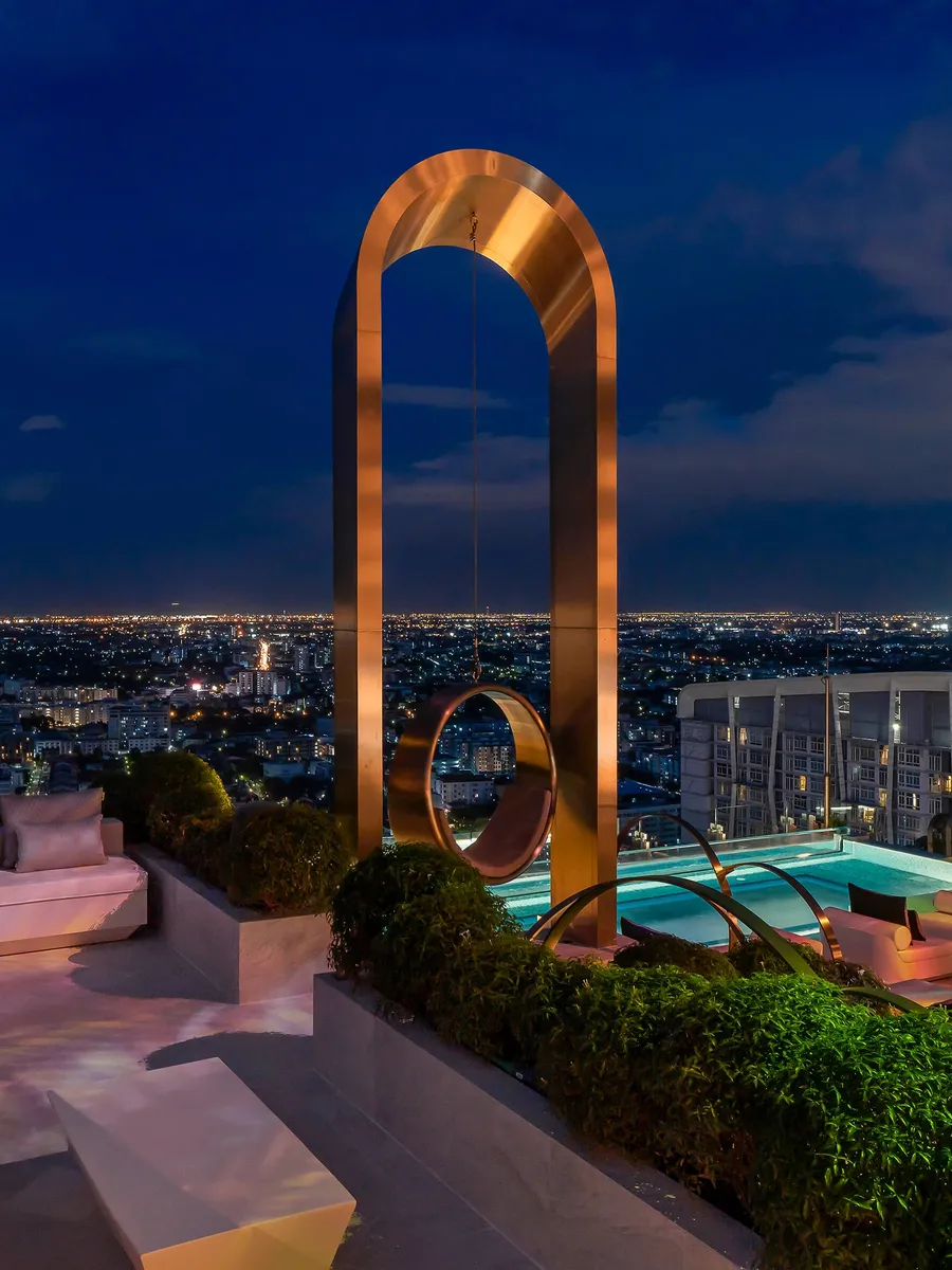 The bronze Giant Swing arch on the pool deck of INNSiDE by Meliá Bangkok Sukhumvit at night, city lights behind