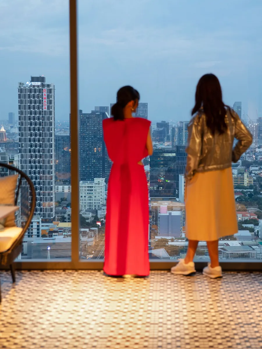 Two guests at the window of LUZ Bangkok Tapas Bar looking over the Sukhumvit skyline at dusk