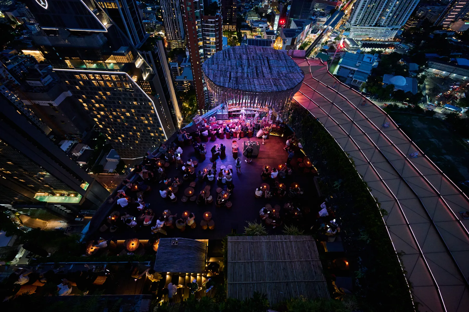 Tichuca's rooftop terrace seen from above at night, tables lit by candles under the round canopy, surrounded by Sukhumvit's towers