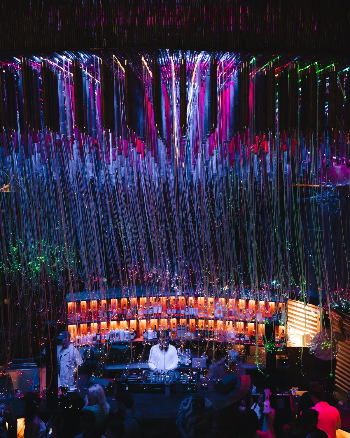 A DJ at the decks under thousands of glowing light strands hanging from Tichuca's canopy, the crowd gathered in front