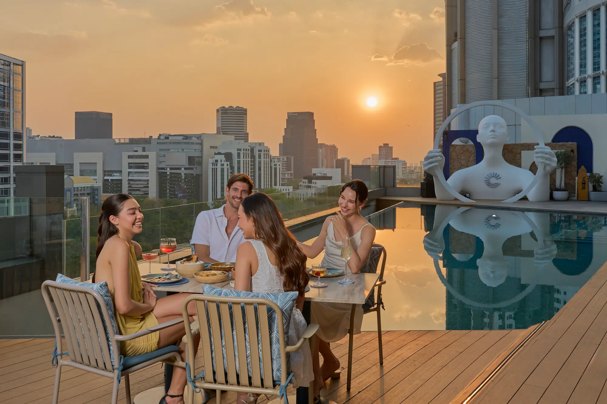 Friends dining at a poolside table during golden hour on the View rooftop, Bangkok